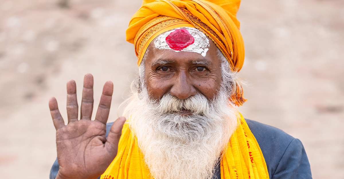Portrait of an old male indian sadhu baba sitting on ghats near river ganges in a blessing pose at varanasi city in traditional dress.