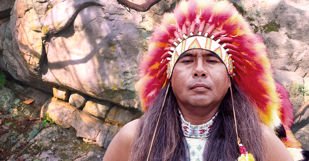 Cherokee man in front of a carved skull rocks