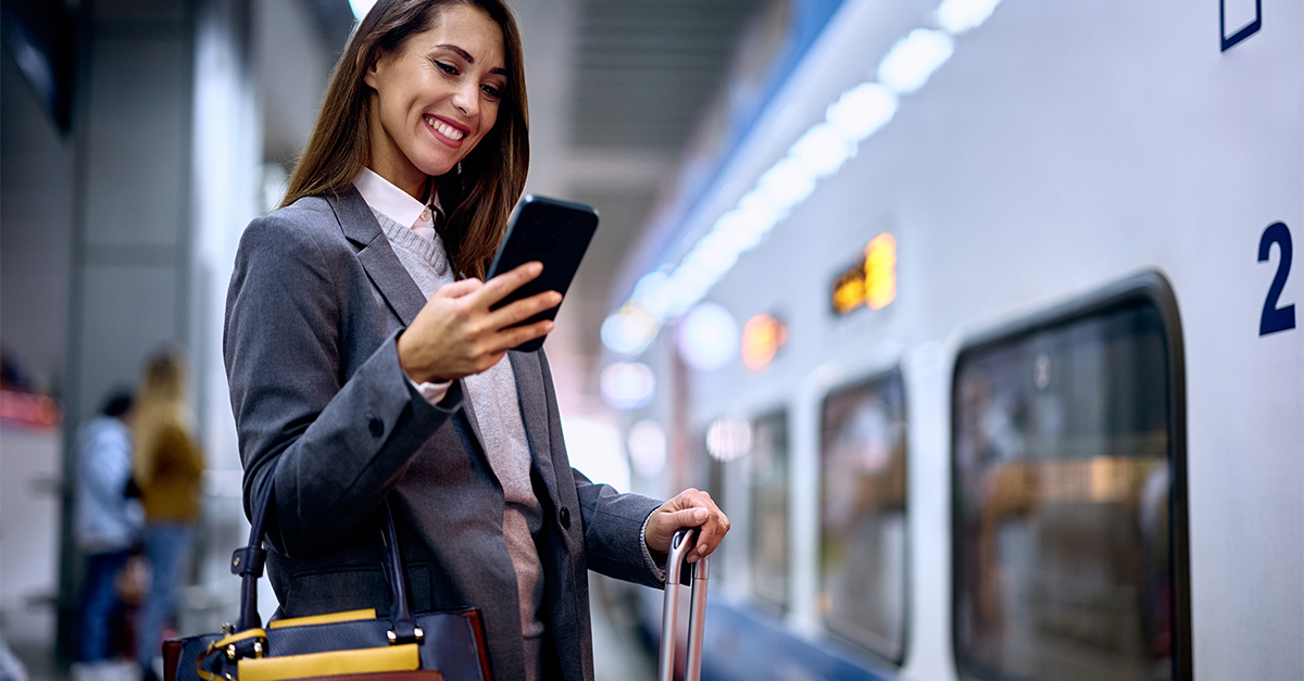 Young happy woman using cell phone while waiting for a train at the station. Copy space.
