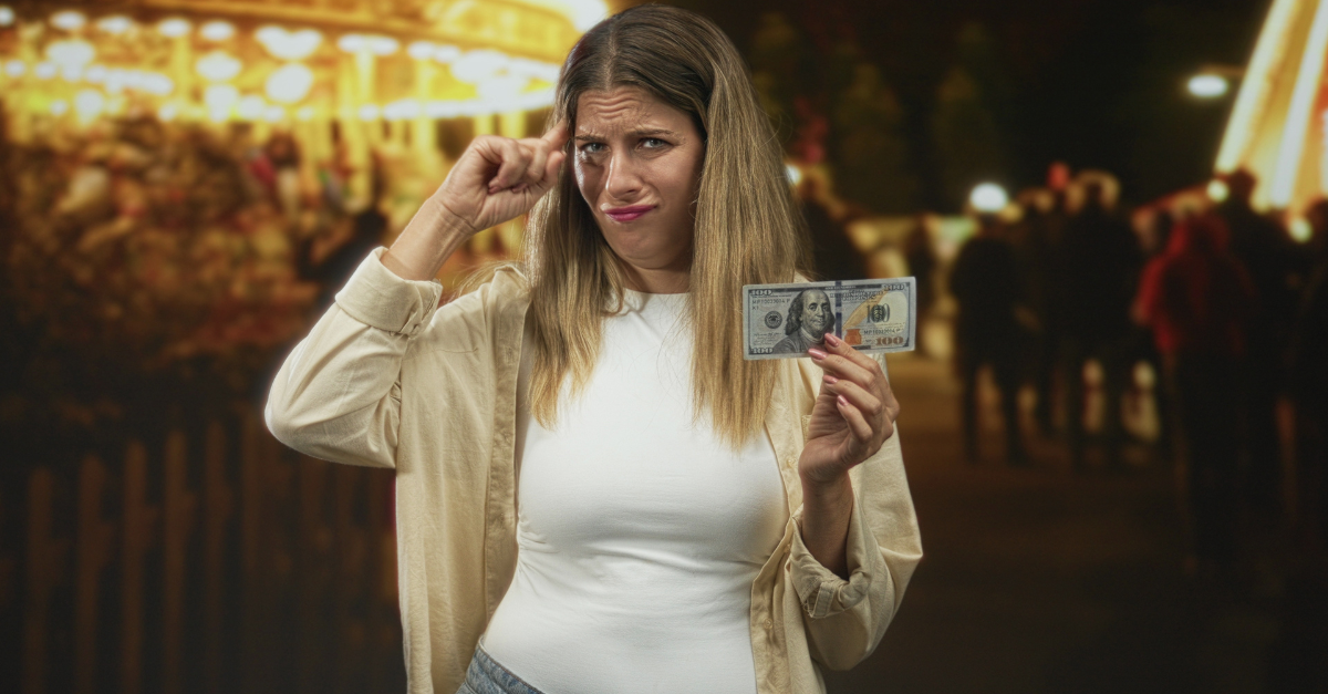 Woman holds a hundred dollar banknote while shrugging shoulders in a busy street fair with carousel lights; confusion uncertainty.