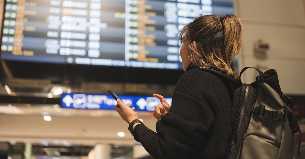 Young Asian woman in international airport looking at flight information board, checking her flight