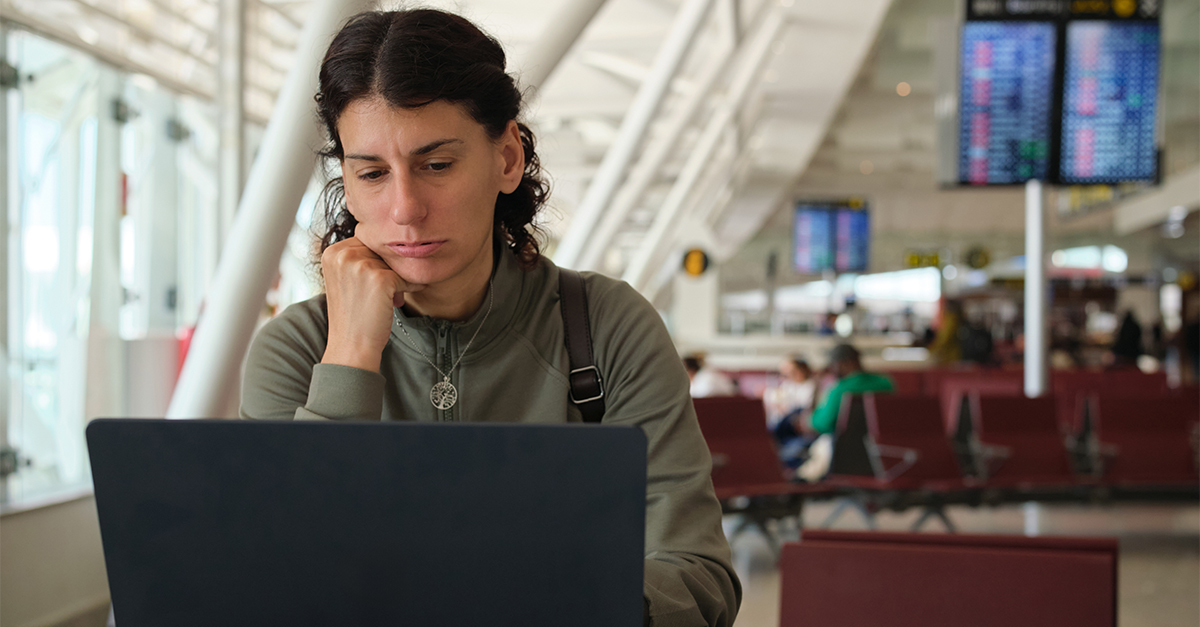 Woman focusing on laptop with a worried expression, sitting at a table with passports in an airport terminal