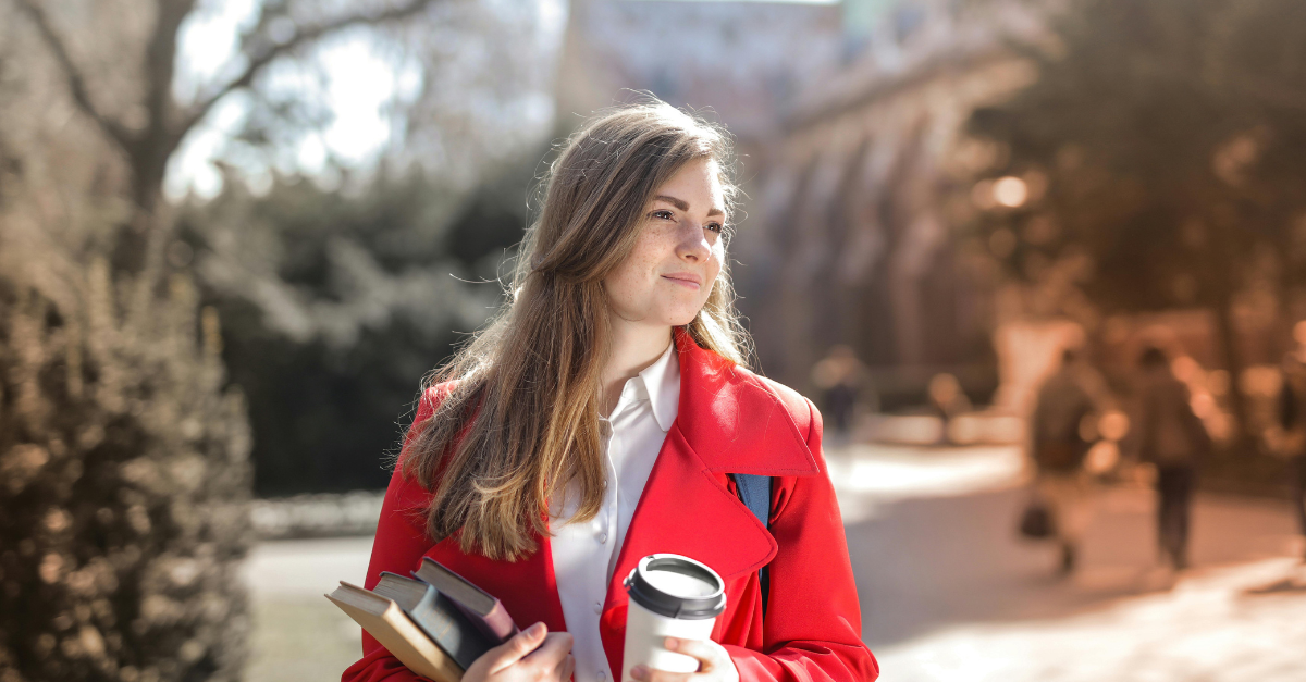 woman-in-red-coat-holding-notebooks-and-coffee-cup-