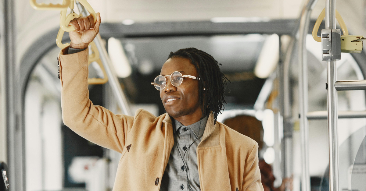 man-in-brown-coat-holding-on-bus-handle-while-holding-a-book