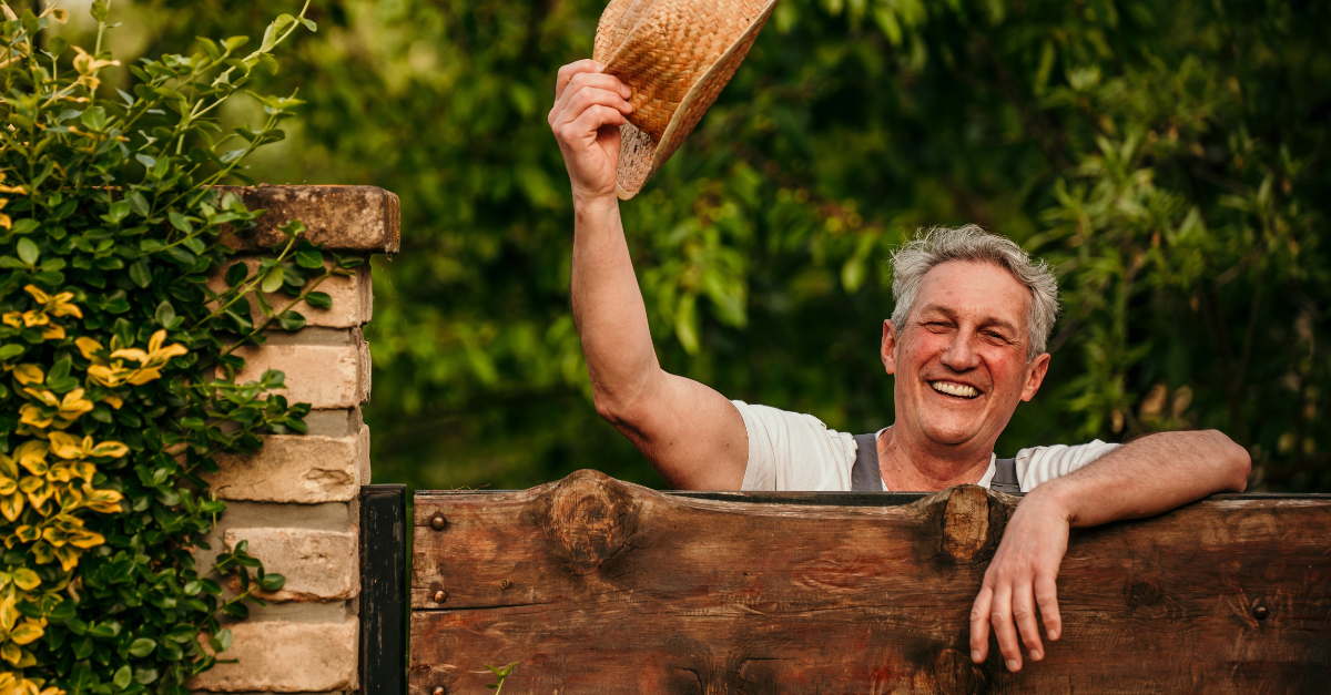 A senior man leaned on the fence in his backyard. Countryside people concept