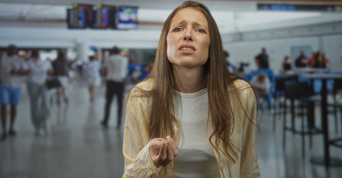 Woman with palm up hand and worried face at airport terminal gesturing complaint; travel delay frustration.