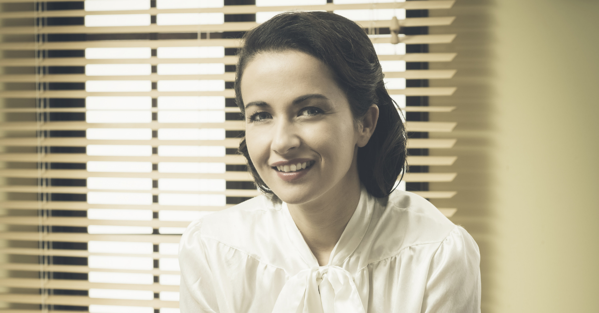 1950s smiling business woman leaning on office desk