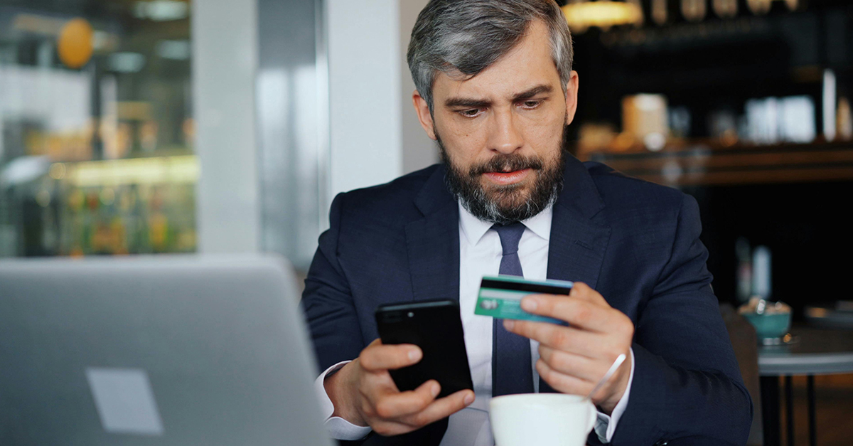 A businessman at a cafe, frowning at his credit card.