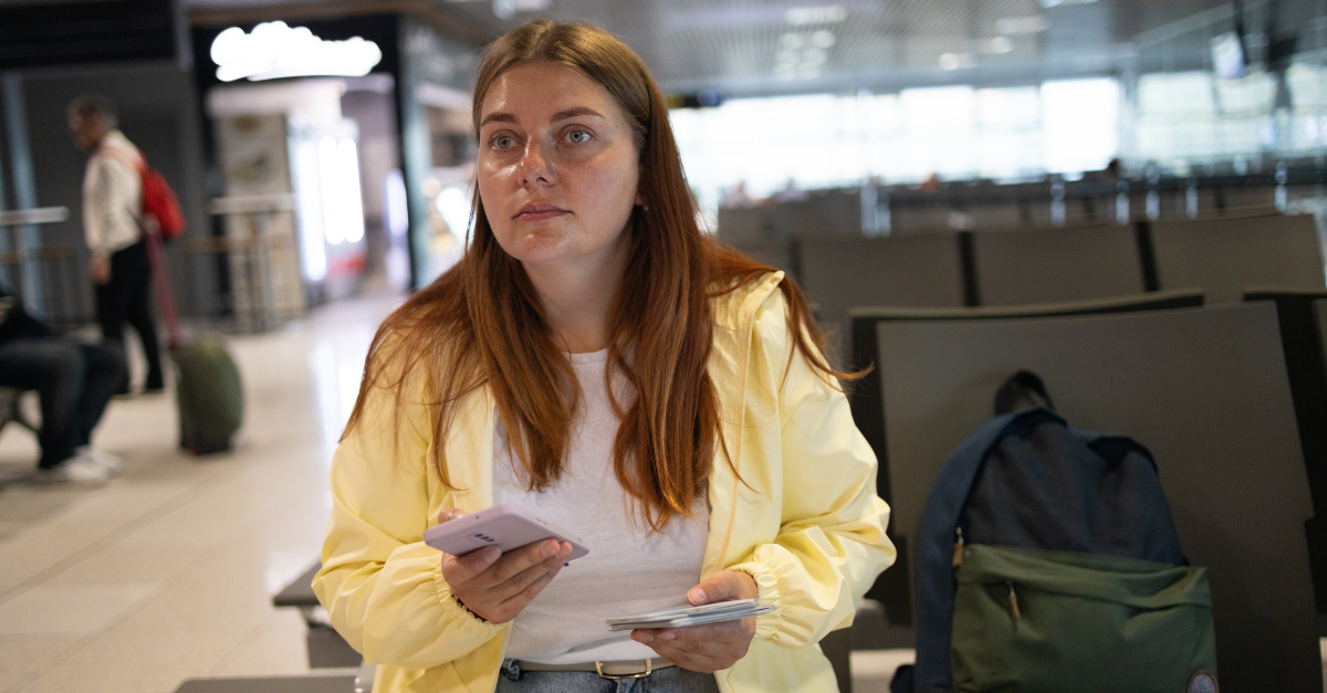 Upset woman using smartphone while waiting for her flight at departure area.