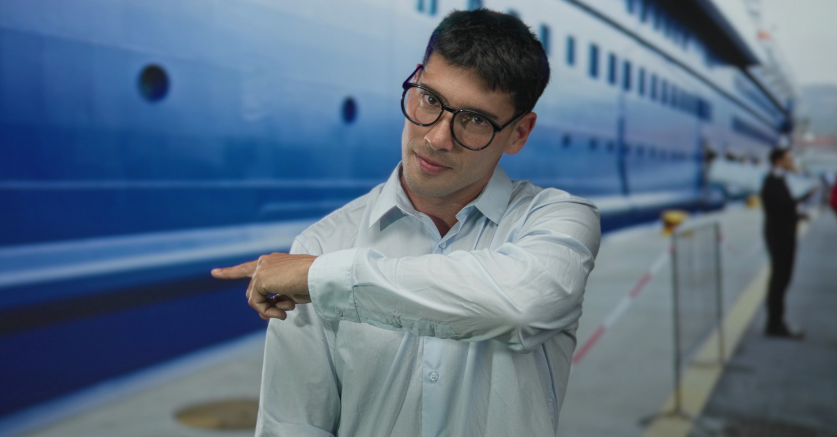 Young hispanic man in glasses wearing blue shirt finger pointing to large ship on street;new journey anticipation.