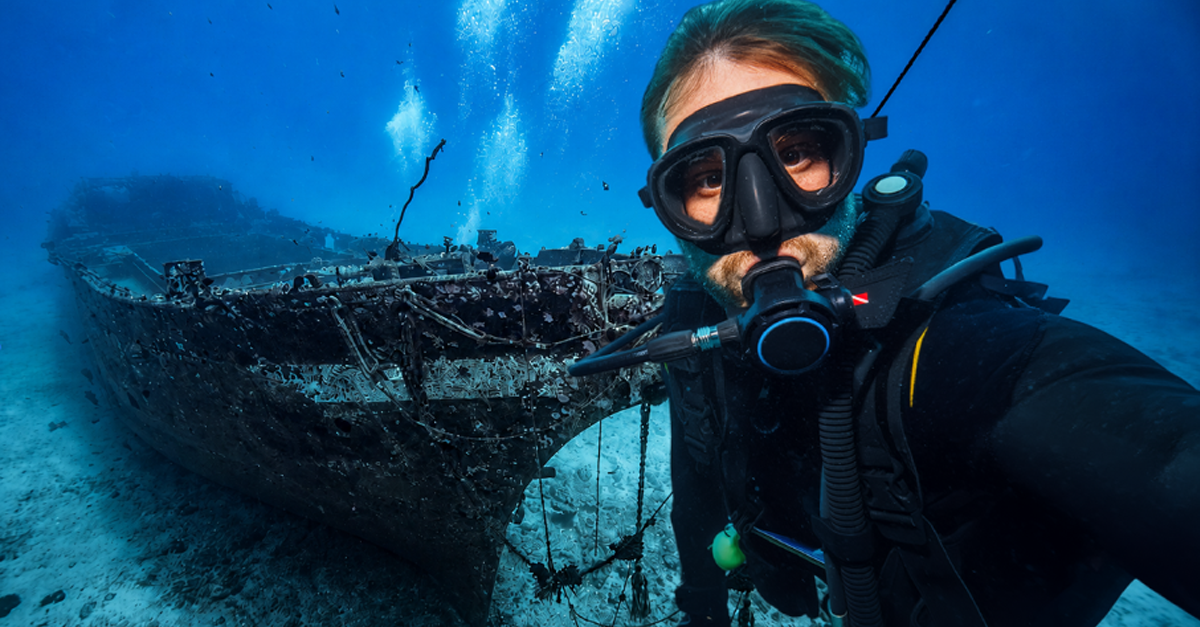Composite of a scuba diver taking a selfie and an underwater shipwreck