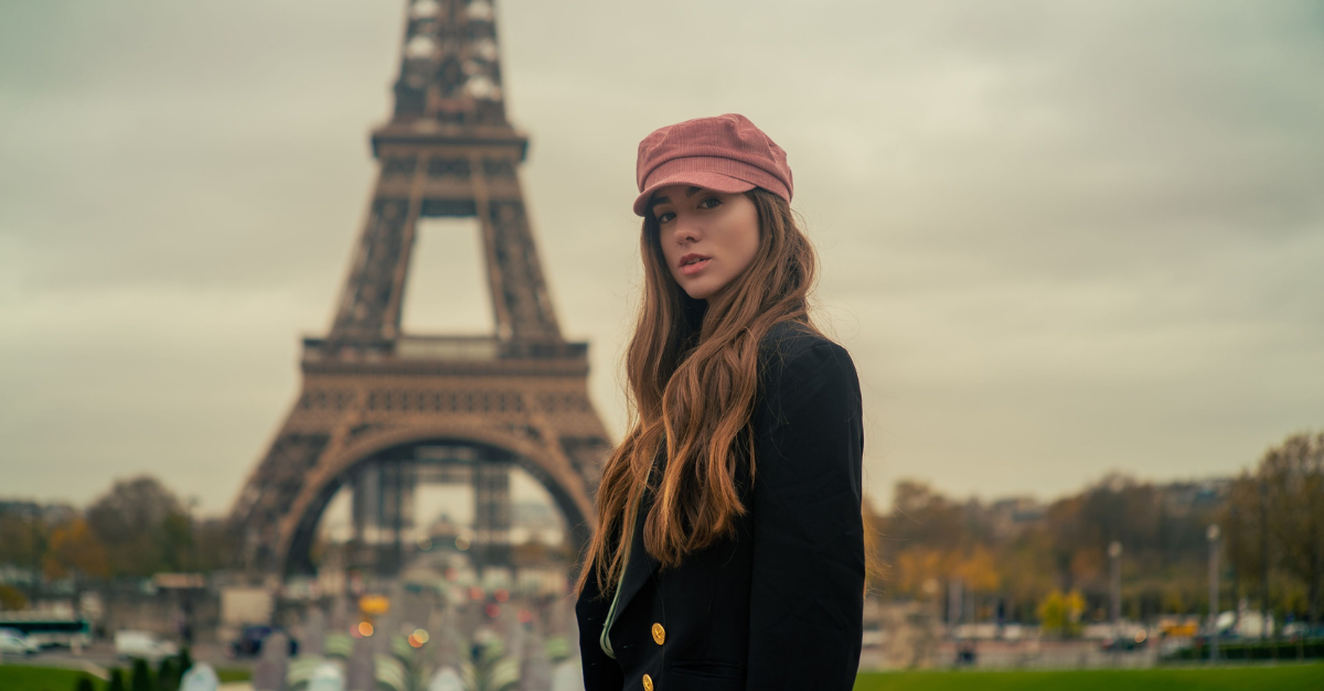 Young woman in a pink cap and black coat poses near the Eiffel Tower in Paris.