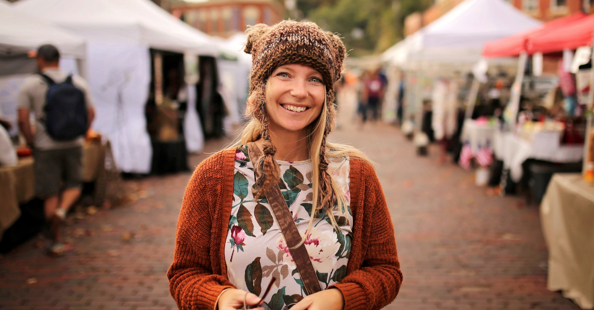 A happy women wearing a hand knit fox winter hat is smiling as she shops outside at a small town fall festival market.