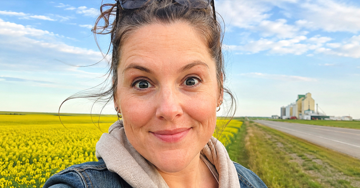 smiling woman with a bun, sunny day, Canadian prairies in the background.