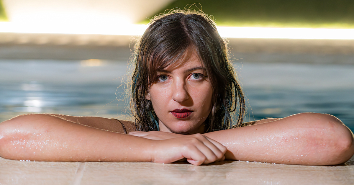 Young woman with wet hair leaning at the side of a pool.