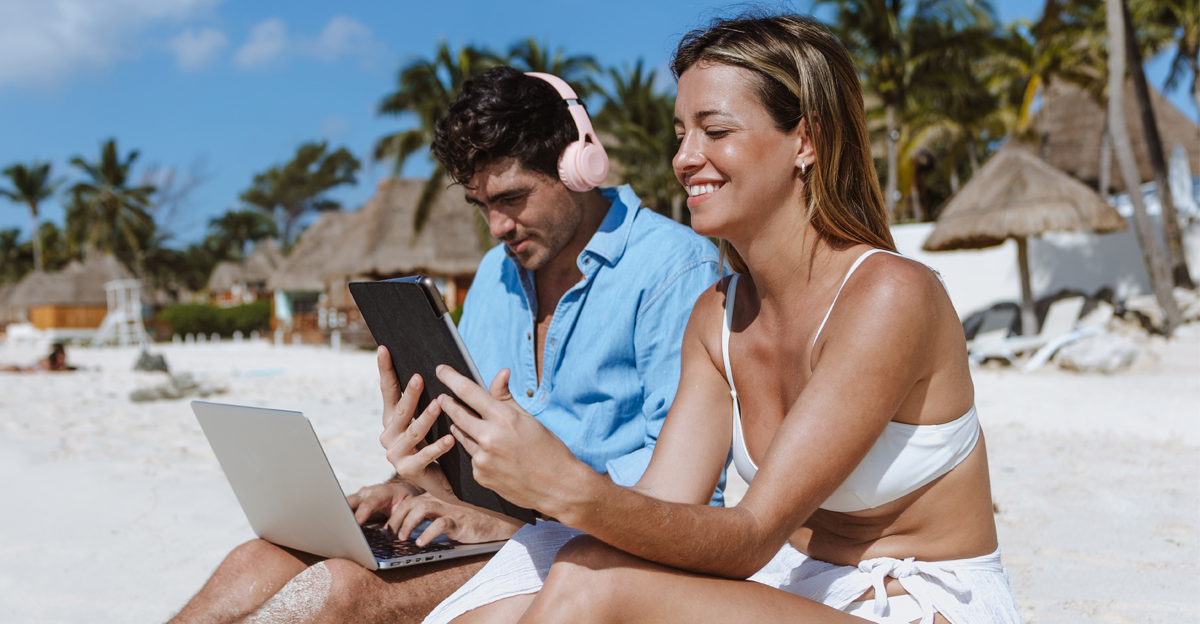 young couple of digital nomads sit down on the beach with laptop and tablet enjoying the travel adventure vacation and working in Mexico Latin America, Caribbean and Tropical destinations